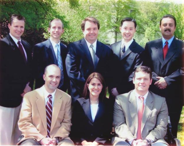 Four men in suits standing behind two men and one woman sitting.